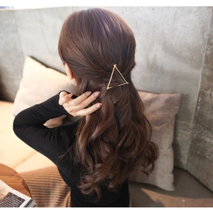 Detail of a minimalist gold triangular metal hair clip worn on a woman's side hair