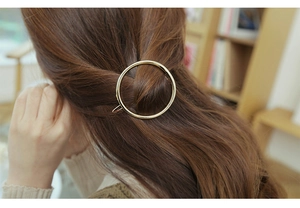 Close-up of golden circular metal hair clip on model with soft indoor lighting