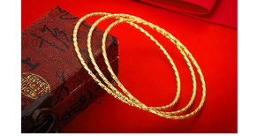 Detail shot of three gold textured bangles with twisted design on a vintage gift box