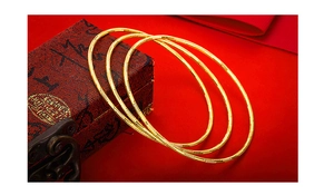 Detailed view of three gold-plated textured bangles on red fabric with a vintage jewelry box