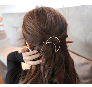 Detail view of a gold crescent moon metal hair clip worn on a woman's wavy hair