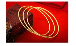 Detailed close-up of three gold-plated bangles with diamond-cut patterns on a red gift box