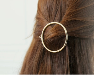 Close-up of a minimalist round gold metal hair clip worn on a model's hair
