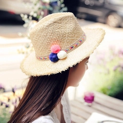 Detail of light beige straw hat featuring boho pom-pom band and fringed brim edge