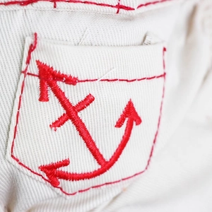 Detail of cream dog onesie featuring red embroidery on a cotton twill pocket