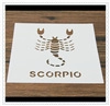 Detail of a white card featuring a brown Scorpio zodiac sign and lettering on wood