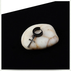Close-up of black stainless steel cross earring on white pebble against dark background