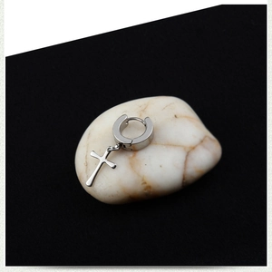 Macro shot of silver stainless steel cross earring on pebbles with high contrast lighting