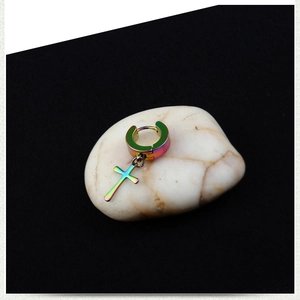 Macro shot of iridescent rainbow cross earring charm on white stones against black background