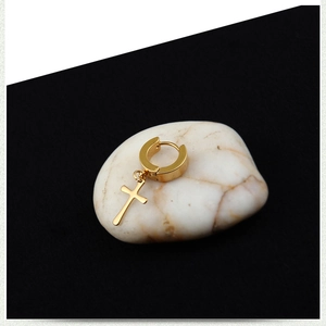 Detail shot of golden cross pendant earring placed on a white pebble with high contrast