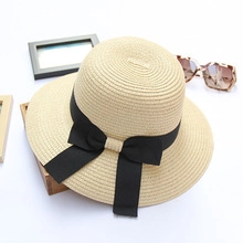 Detail of beige straw sun hat featuring a wide black ribbon bow and textured weave
