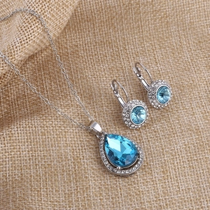 Macro shot of silver teardrop pendant and circular blue crystal earrings set on linen