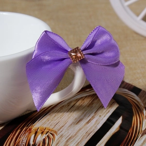 Purple satin ribbon bow with amber square rhinestone displayed on a white coffee cup