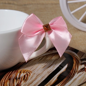 Pink satin bow accessory with a central square amber gemstone on a white cup