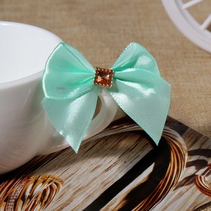 Detail of mint green satin bow hair accessory with square amber rhinestone on white cup