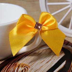 Macro shot of yellow satin bow hair accessory featuring a centered brown rhinestone