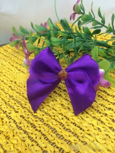 Detail of purple satin bow hair accessory with center amber gemstone on yellow mat
