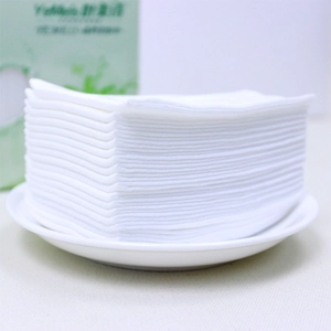 Stack of thick disposable cotton facial towels in a tray for skin cleansing