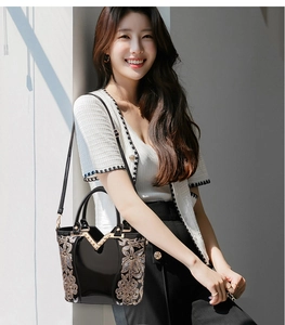 Détail d'un sac à main en cuir verni noir avec broderie florale dorée et boucle à perles