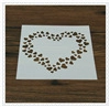 Detailed view of square white plastic coffee stencil with hollow heart patterns on wood