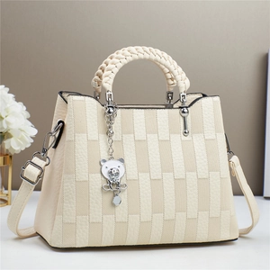 Detail of cream crossbody bag featuring textured geometric patchwork and silver bear charm