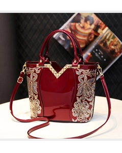 Détail du sac rouge en cuir verni avec broderie florale dorée et ornement en V scintillant