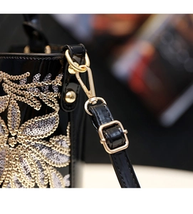 Vue macro détaillée du fermoir doré et des broderies à paillettes sur cuir verni noir