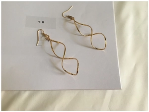 Detailed view of long gold spiral twist earrings with wave curved design and ear hooks