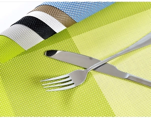 Detail of woven PVC placemat set with a metal knife and fork on a green textured surface
