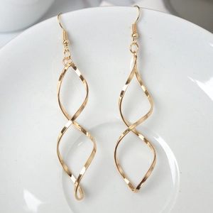 Macro shot of gold spiral twist earrings hanging on a white ceramic plate edge