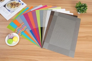Detailed view of woven PVC placemats in various colors displayed on a wooden table