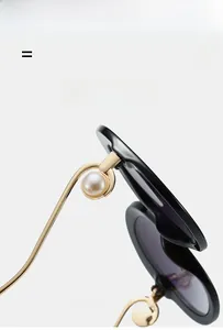 Detail of elegant black sunglasses showing a large pearl accent on golden metal temples