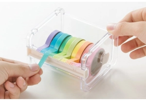 Transparent acrylic washi tape dispenser showing hand pulling tape from a stacked organizer