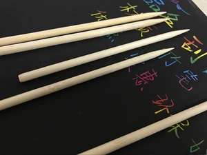 Detailed macro of dual-tip bamboo scratch art tools on a black scratch board surface