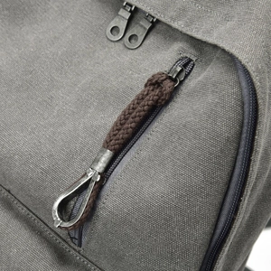 Close-up of grey canvas backpack featuring vintage metal hooks and brown cotton rope pulls