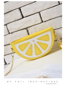 Vibrant lemon slice crossbody bag with golden chain strap on a white brick background