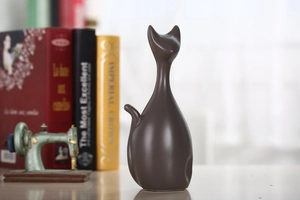 Detail van matbruine keramieken kattenbeeldje met boeken en een naaimachinemodel