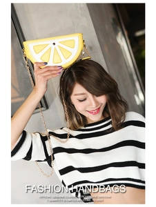 Detail view of a lemon-shaped yellow crossbody bag with chain strap worn as a headpiece