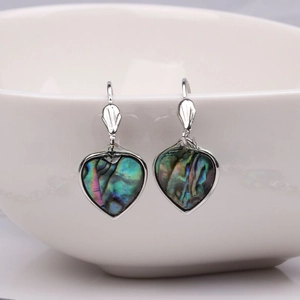 Detail of heart-shaped abalone shell earrings hanging on a white ceramic bowl edge