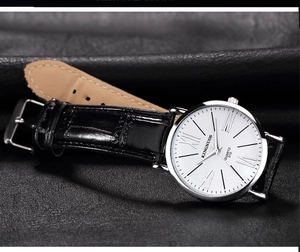 Close-up of KINGNUOS quartz watch with white dial and black leather strap on dark background