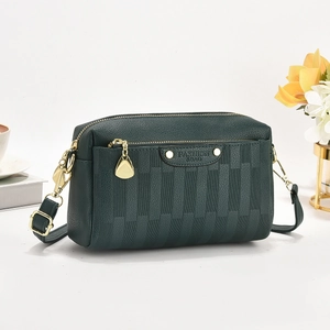 Macro detail of dark green pebbled leather handbag with gold zipper and metal plate