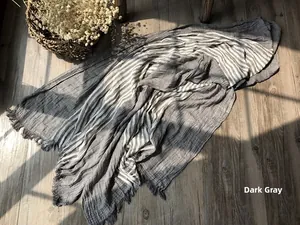 Detail of dark grey striped cotton scarf showing soft texture and tassel edges on wood