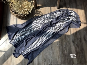 Detail of navy blue and white striped cotton scarf with fine fringe on wooden surface