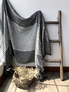 Detailed view of grey and white striped cotton scarf with fringed edges on wooden ladder