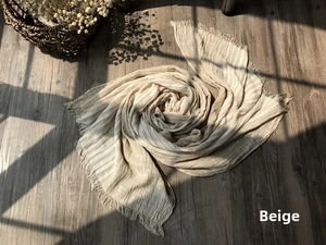 Detail of beige striped cotton scarf with fine fringes on dark wooden floor