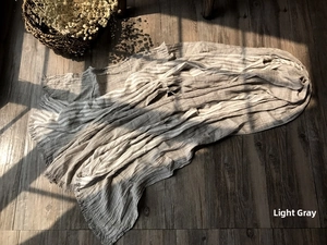 Light gray cotton linen scarf with fringe edges shown on a rustic wooden floor