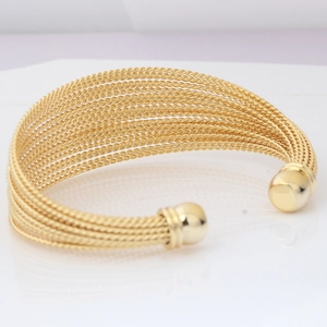 Detail of golden multi-layer twisted cable cuff bracelet with spherical ends on white surface