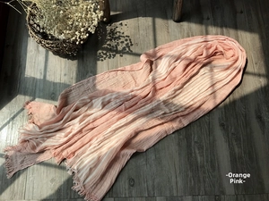 Detail of orange pink striped cotton scarf with natural fringe on dark wood background