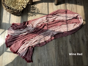 Close-up of wine red and beige striped cotton scarf with fringe on wood background