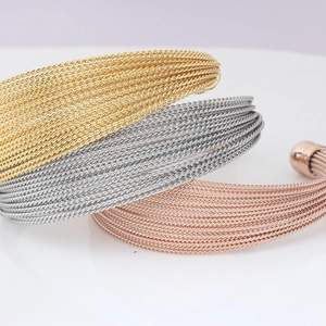 Detailed macro view of triple-layered twisted cable open bangles in gold, silver, and rose gold